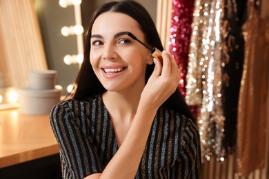 Beautiful young woman applying mascara in dressing room