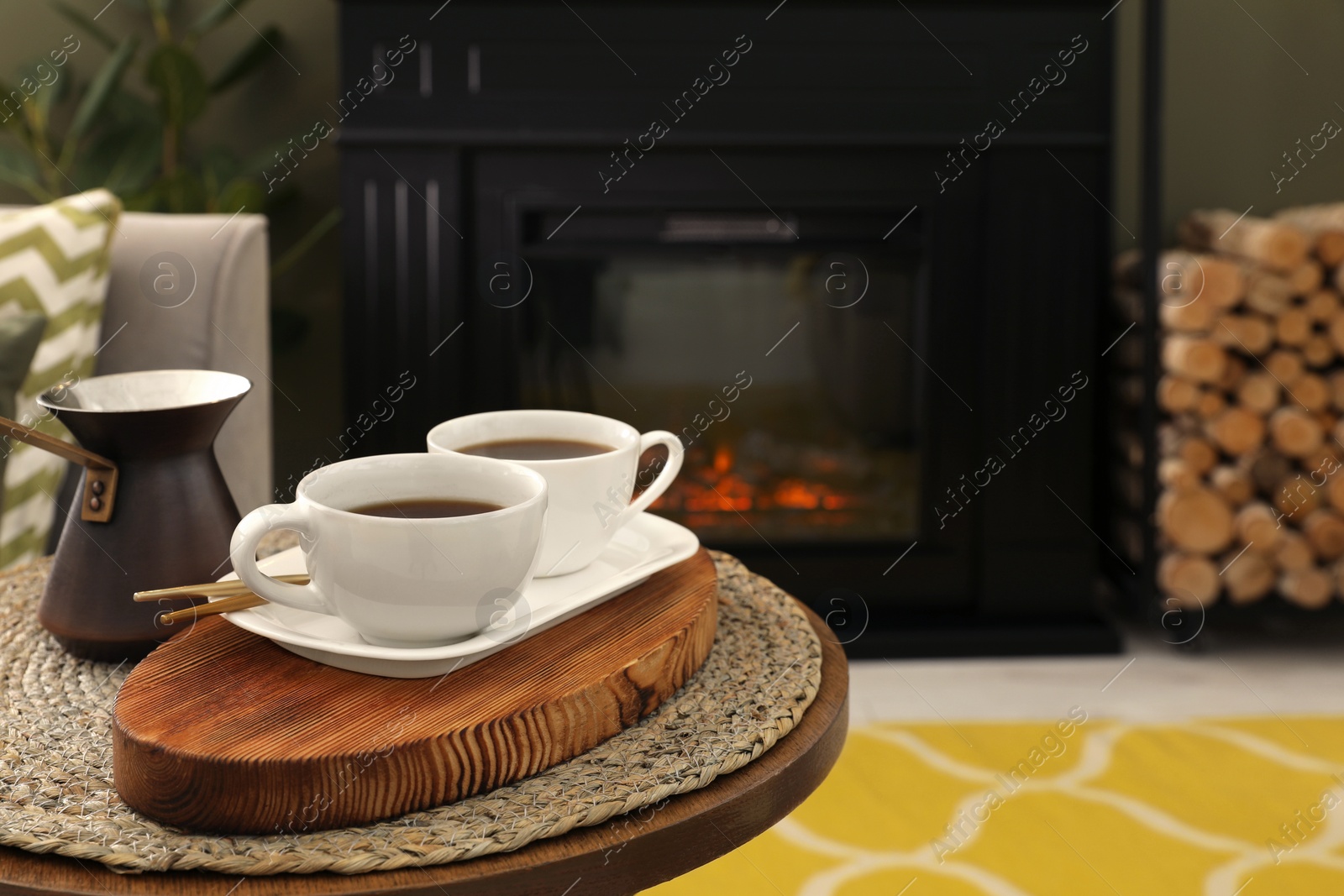 Photo of Cups of coffee and cezve on table near fireplace in living room