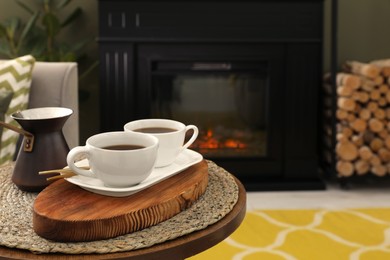 Cups of coffee and cezve on table near fireplace in living room