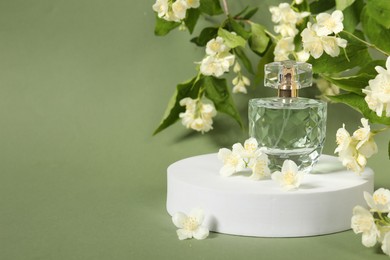 Photo of Presentation of aromatic perfume in bottle and beautiful jasmine flowers against pale green background, space for text