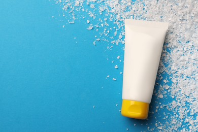 Photo of Tube of hand cream and decorative snow on light blue background, flat lay with space for text. Winter skin care