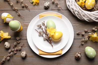 Festive Easter table setting with painted eggs and floral decor on wooden background, flat lay