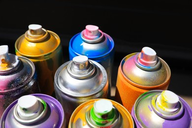 Photo of Used cans of spray paint on dark background, closeup. Graffiti supplies