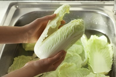 Photo of Woman washing fresh Chinese cabbages in sink, closeup