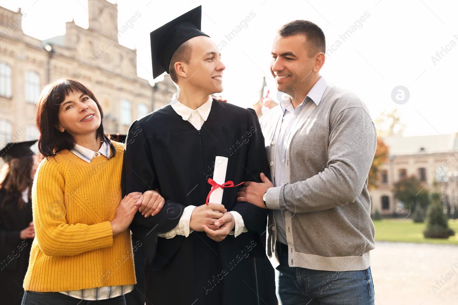 Photo of Happy student with parents after graduation ceremony outdoors