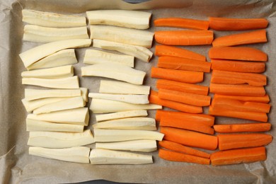 Baking tray with parchment, parsnips and carrots, top view