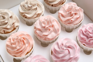 Photo of Many tasty cupcakes with colorful cream in box, closeup