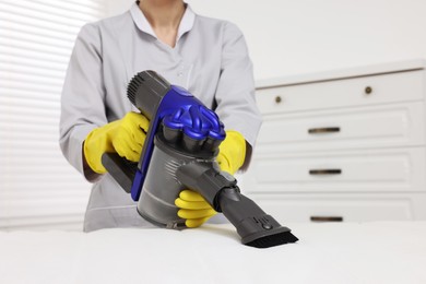 Photo of Woman in gloves disinfecting mattress with vacuum cleaner indoors, closeup. Space for text