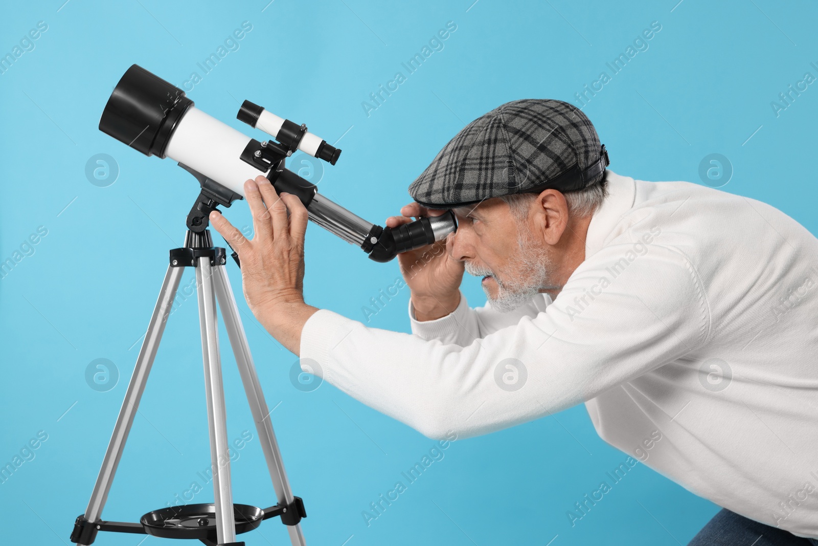 Photo of Senior astronomer looking at stars through telescope on light blue background