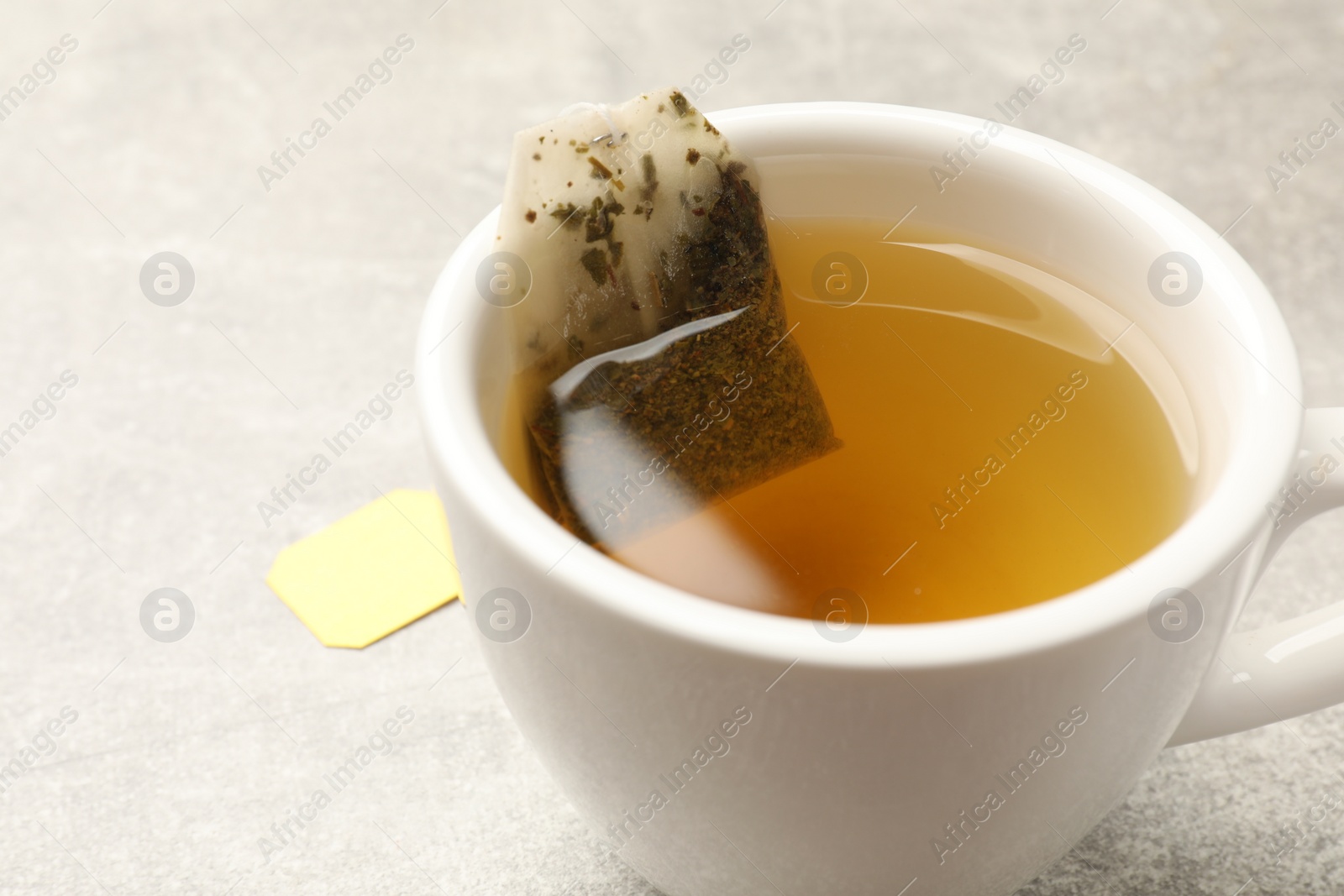 Photo of Brewing tea. Cup with tea bag on light table, closeup. Space for text