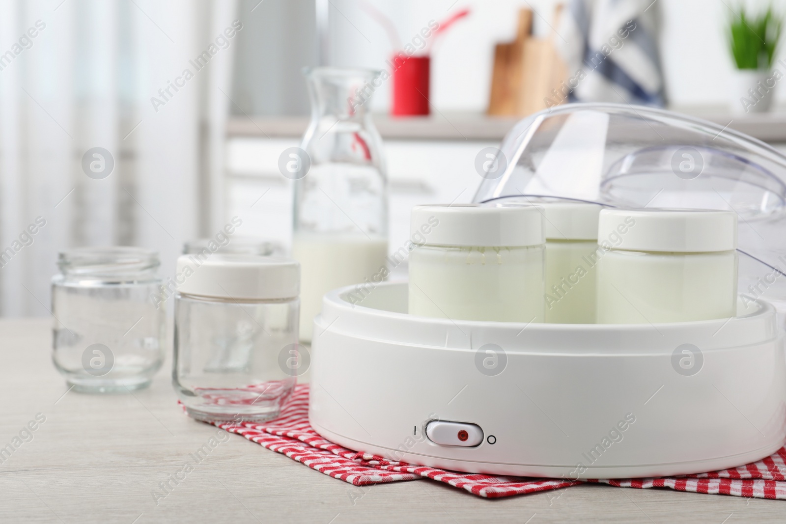 Photo of Modern yogurt maker and jars on wooden table in kitchen