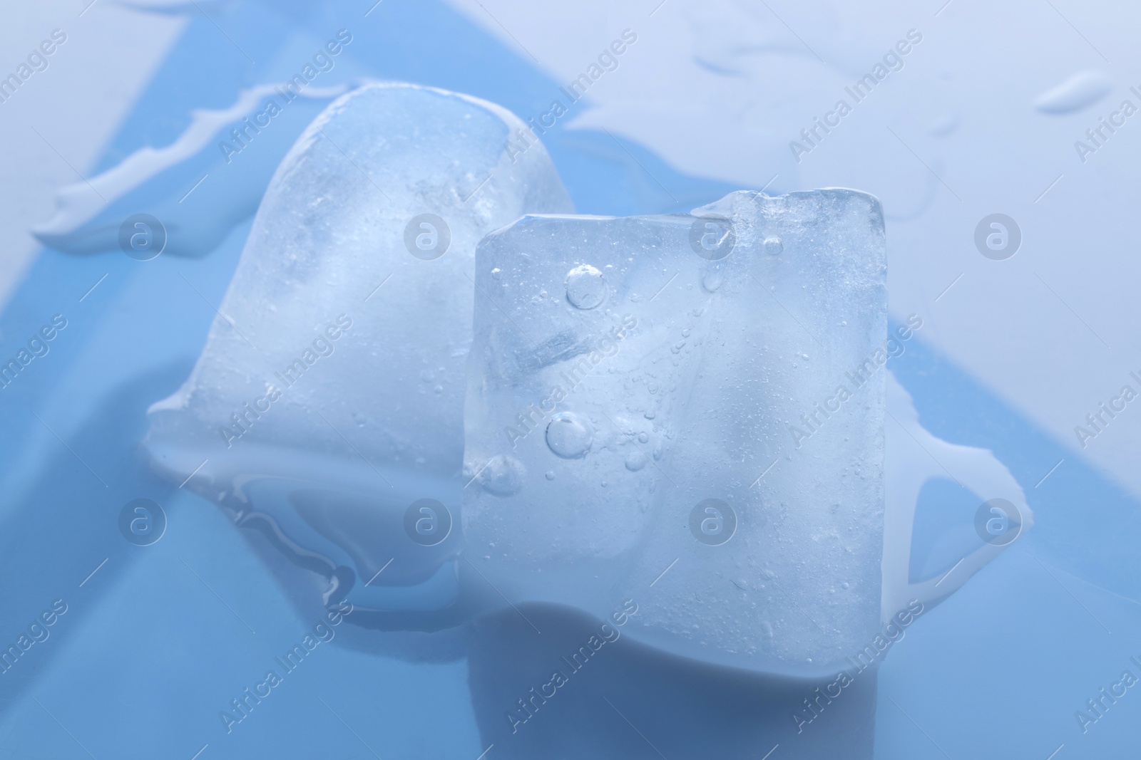 Photo of Crystal clear ice cubes on light blue background, closeup