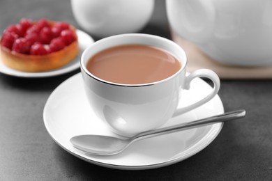 Photo of Delicious tea with milk in white cup near dessert on grey table