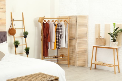 Stylish wooden table and rack with clothes in modern bedroom interior