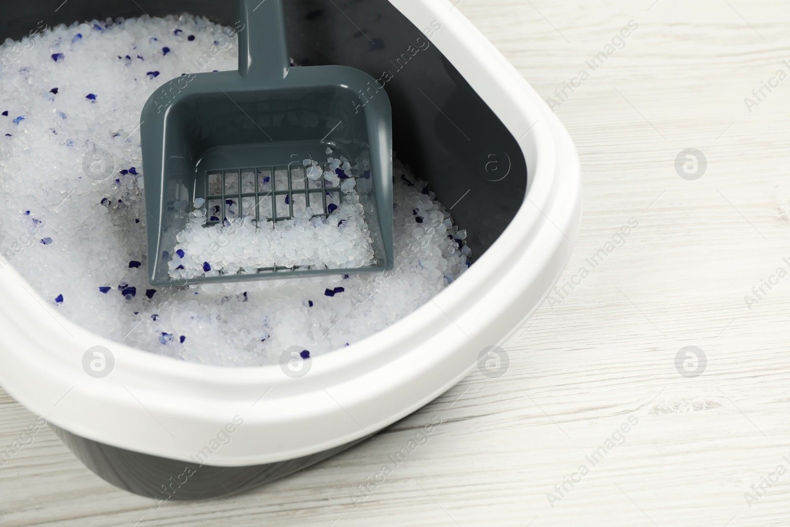 Photo of Cat litter tray with filler and scoop on white wooden floor, closeup