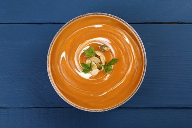 Photo of Delicious pumpkin soup with seeds and parsley in bowl on blue wooden table, top view