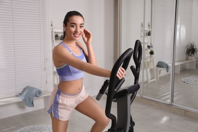 Happy young woman training on elliptical machine at home