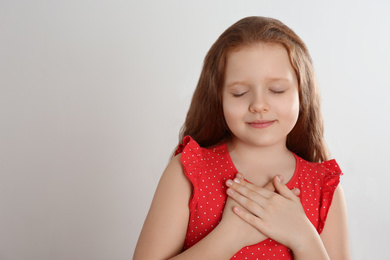 Photo of Cute grateful little girl with hands on chest against light background