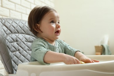 Cute little baby sitting in high chair indoors