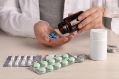 Different pills in blisters on white wooden table, woman with bottle, selective focus