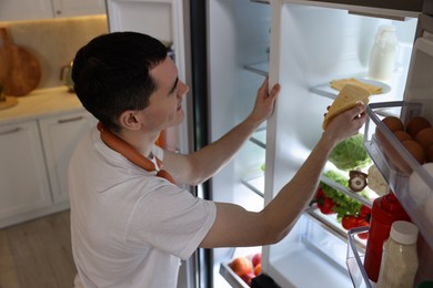 Photo of Man with sausages taking cheese out of refrigerator in kitchen, above view