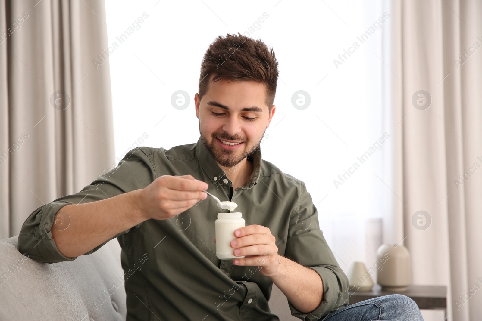 Photo of Happy young man with tasty yogurt in living room