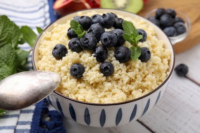 Bowl of tasty couscous with blueberries and mint served on white table, closeup