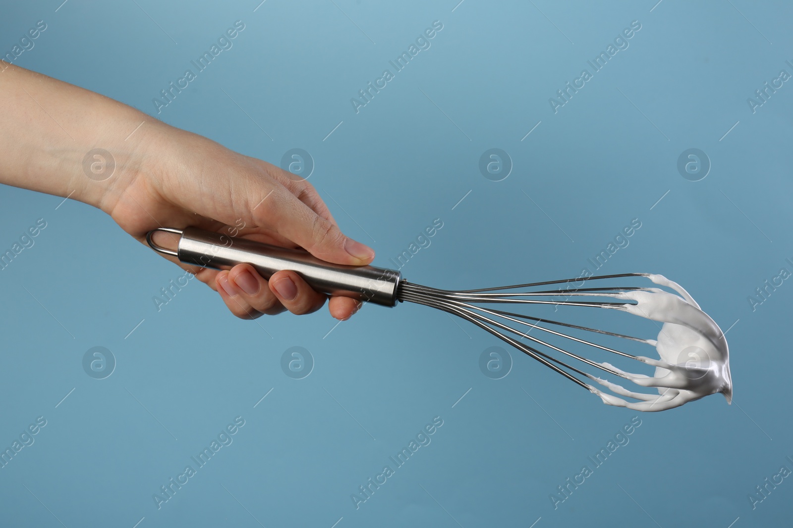 Photo of Woman holding whisk with whipped cream on light blue background, closeup