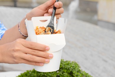 Woman eating takeaway noodles from paper box with fork outdoors, closeup and space for text. Street food