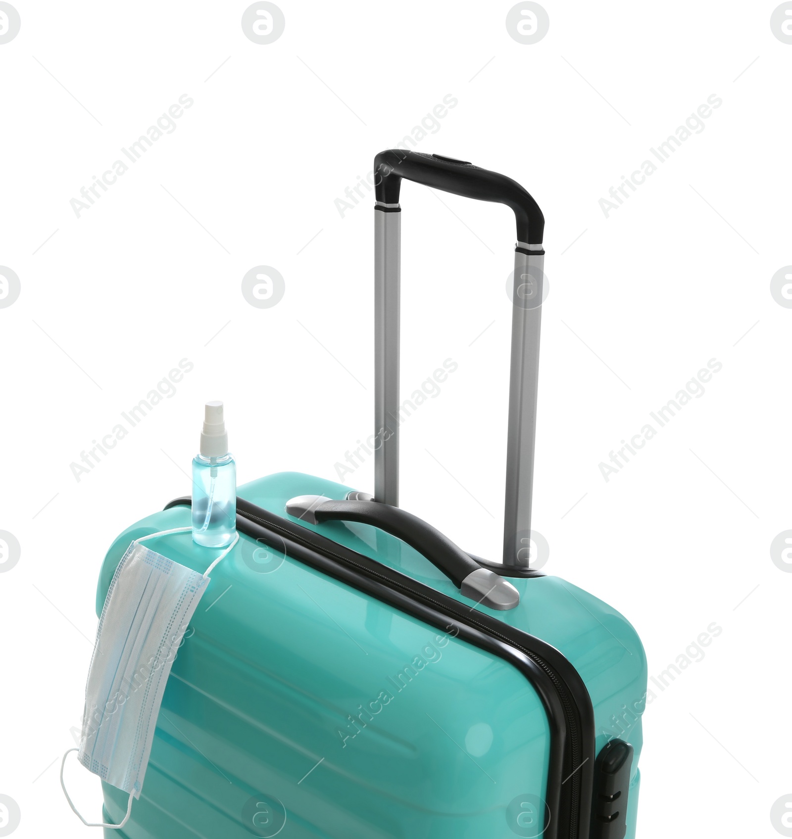 Photo of Stylish turquoise suitcase, antiseptic spray and protective mask on white background. Travelling during coronavirus pandemic