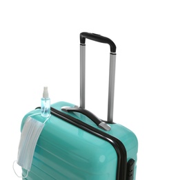 Photo of Stylish turquoise suitcase, antiseptic spray and protective mask on white background. Travelling during coronavirus pandemic