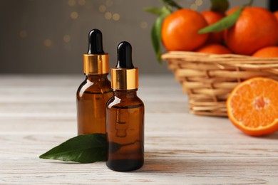 Bottles of tangerine essential oil and green leaf on white wooden table, closeup