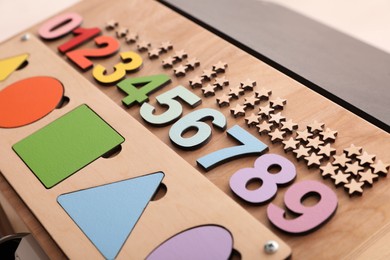 Photo of Busy board with colorful numbers and shapes on light background, closeup. Baby sensory toy
