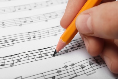 Photo of Woman writing music notes on sheet with pencil, closeup