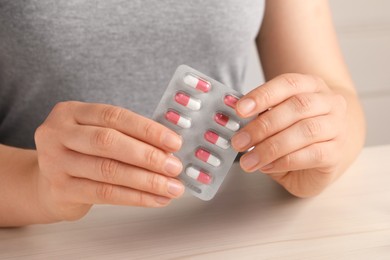 Photo of Woman holding blister of pills at white wooden table, closeup