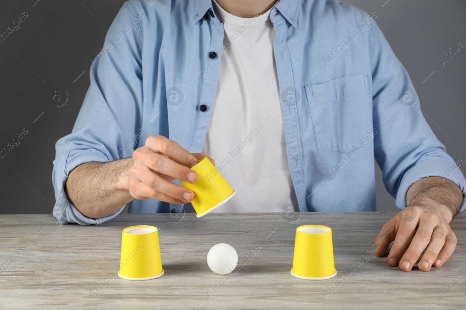 Photo of Shell game. Man showing ball under cup at wooden table, closeup