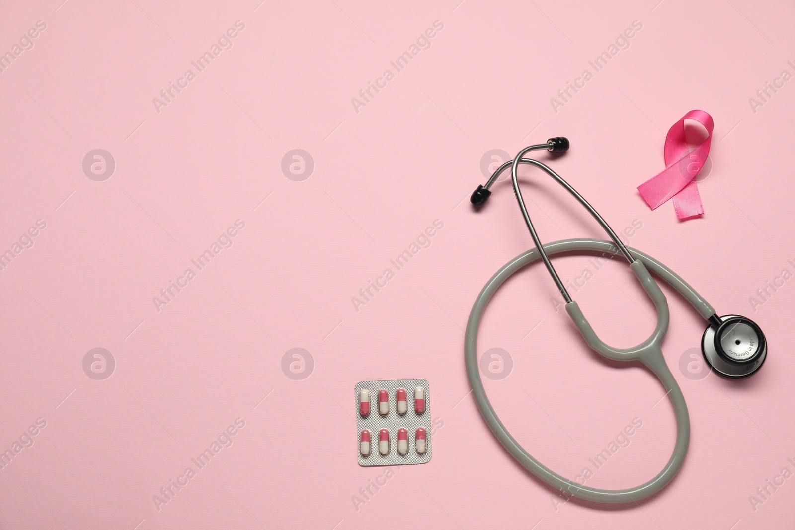 Photo of Breast cancer awareness. Pink ribbon, stethoscope and pills on color background, flat lay. Space for text