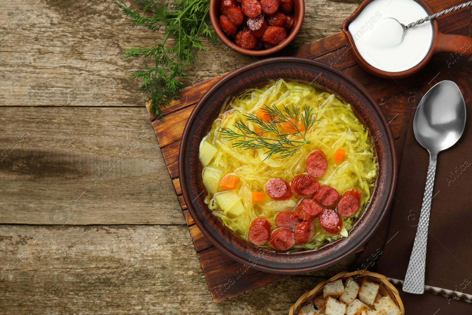Photo of Delicious sauerkraut soup with smoked sausages and dill served on old wooden table, flat lay. Space for text