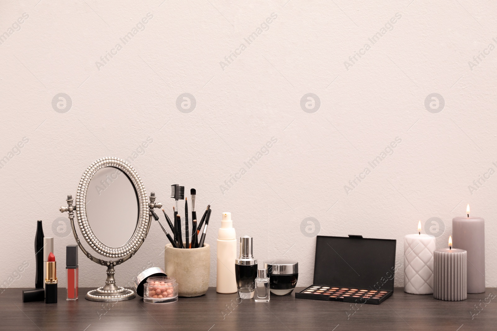 Photo of Mirror, candles and different makeup products on dark wooden dressing table near wall