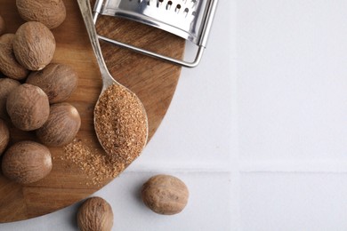 Spoon with grated nutmeg, seeds and grater on white table, flat lay. Space for text