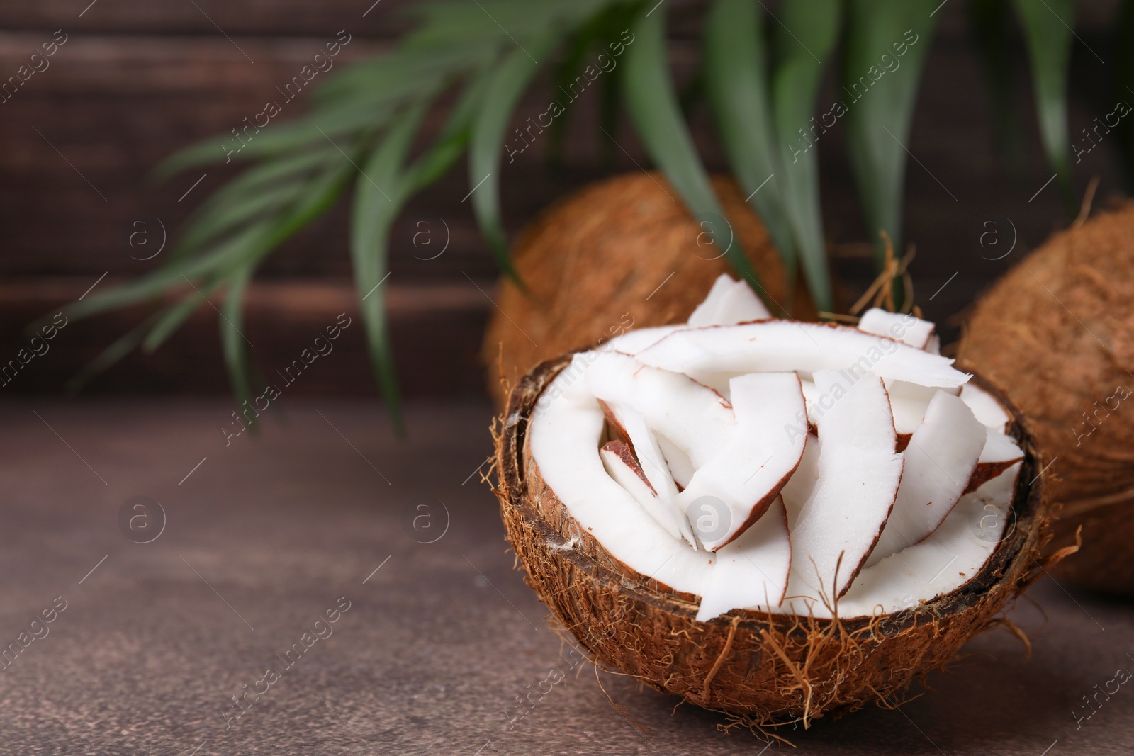 Photo of Coconut pieces in nut shell on brown table, space for text