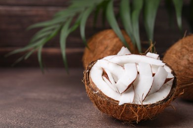 Coconut pieces in nut shell on brown table, space for text