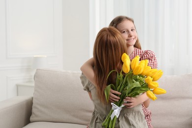 Photo of Daughter congratulating mom with bouquet of yellow tulips at home, space for text