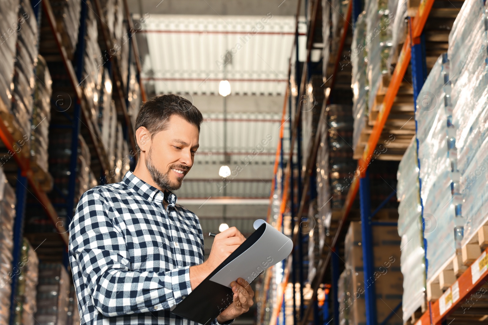 Photo of Happy manager holding clipboard in warehouse with lots of products., low angle view