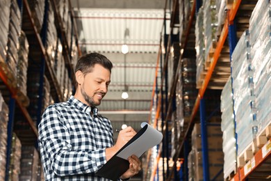 Happy manager holding clipboard in warehouse with lots of products., low angle view