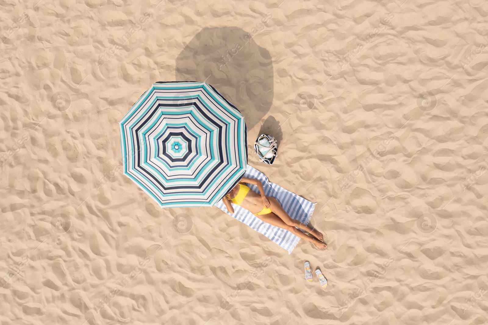 Image of Woman resting under striped beach umbrella at sandy coast, aerial view