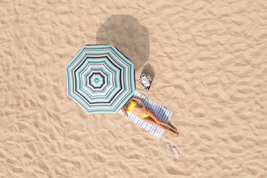 Woman resting under striped beach umbrella at sandy coast, aerial view