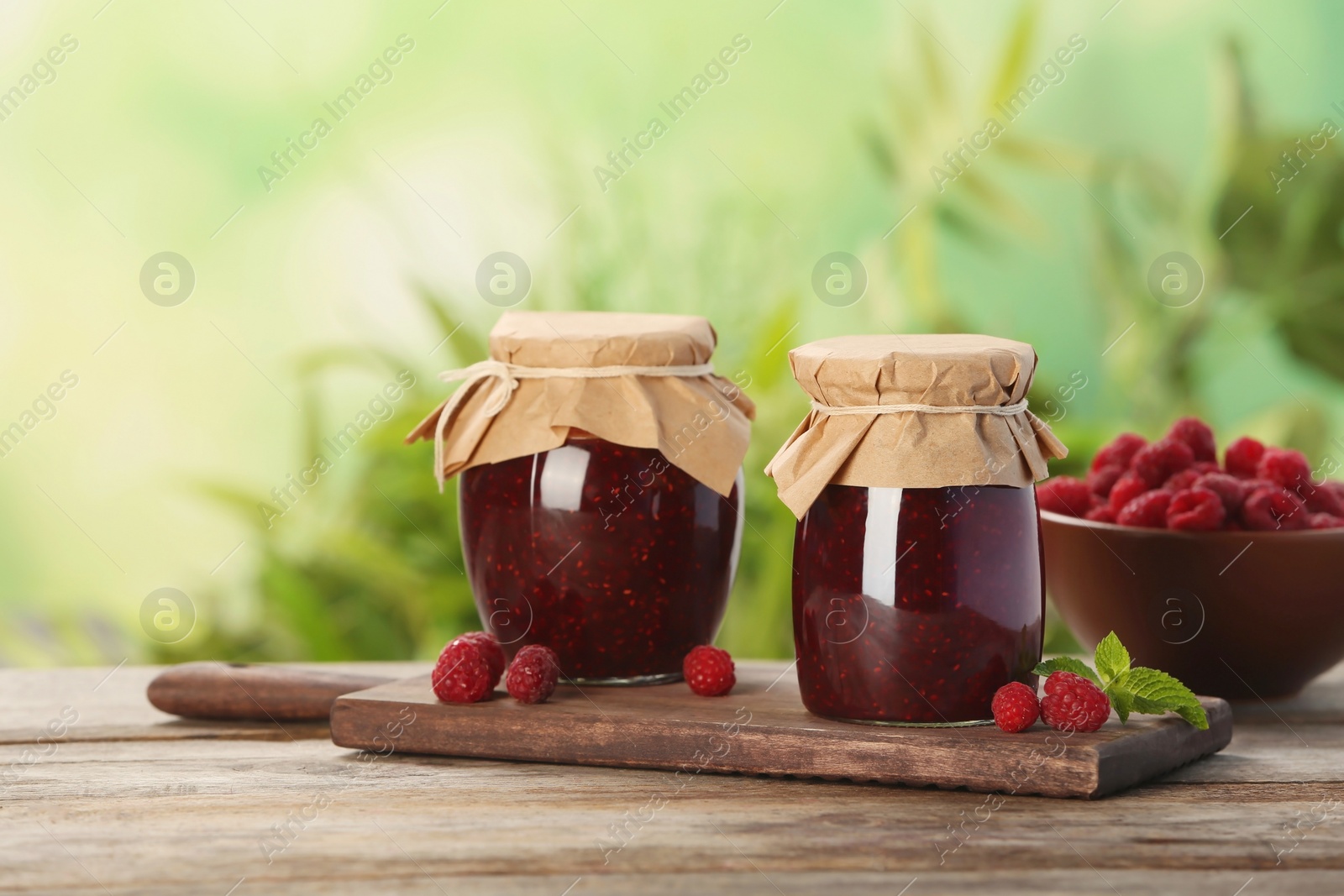 Photo of Jars with delicious raspberry jam on table against blurred background