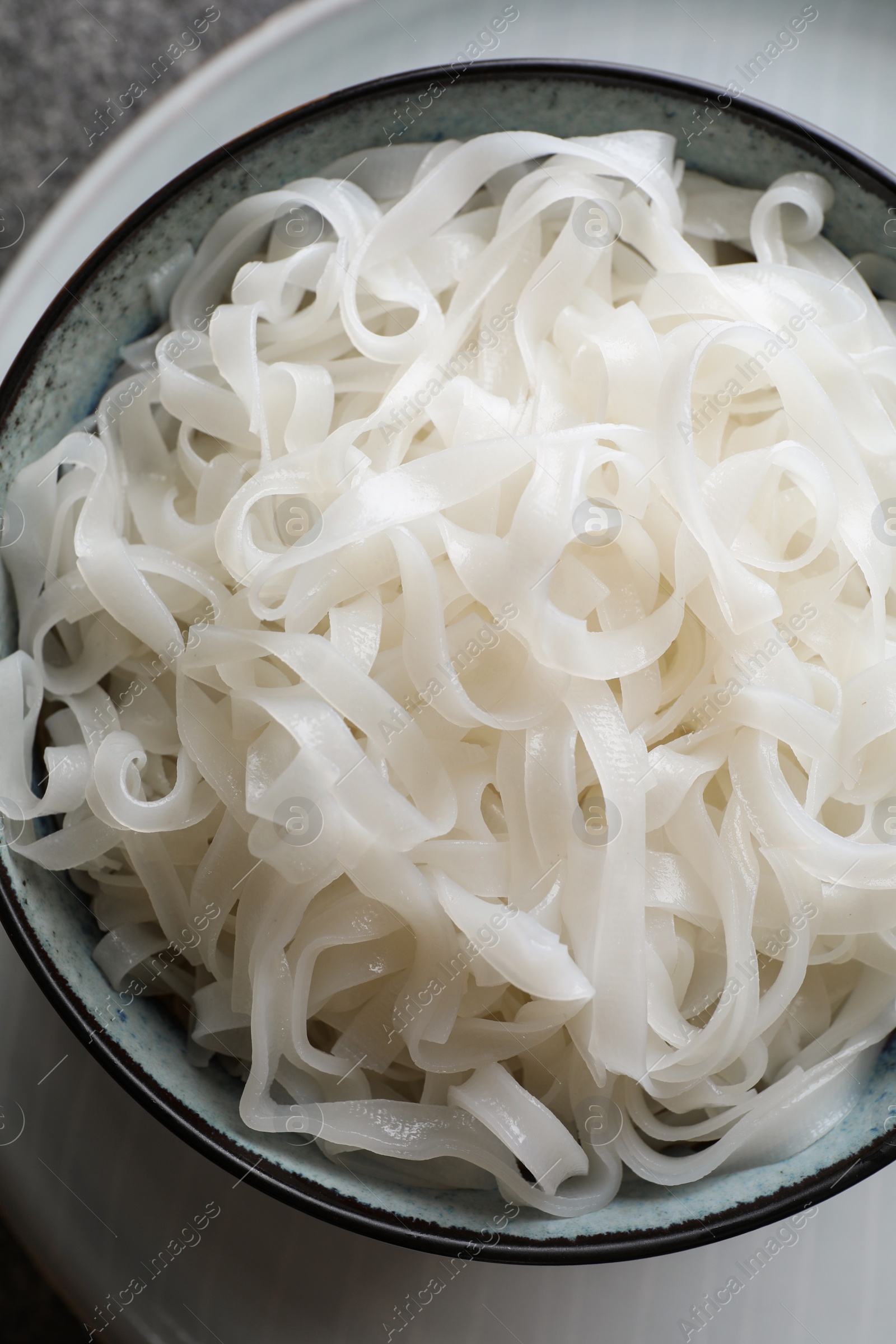 Photo of Bowl of tasty cooked rice noodles on grey table, top view