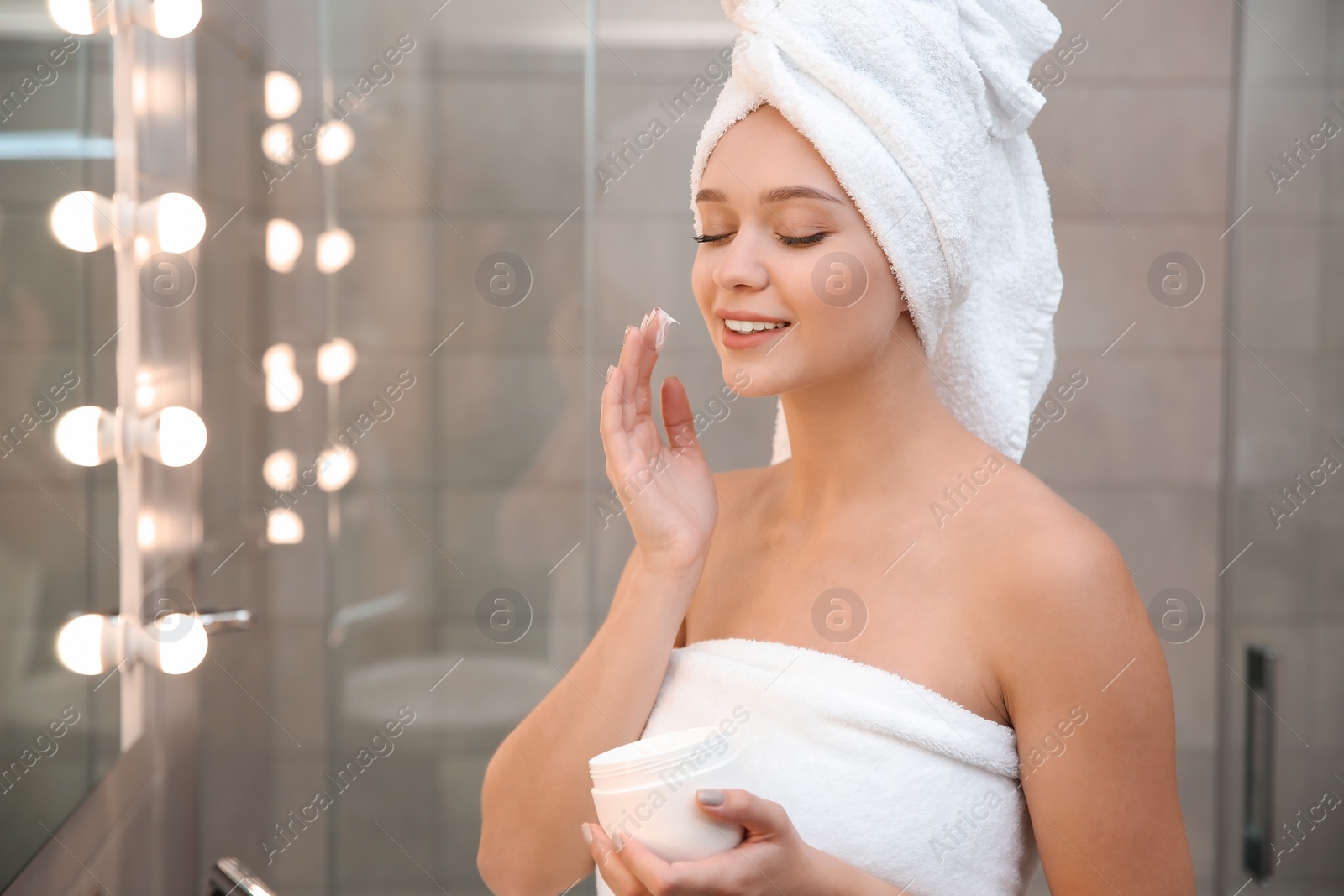 Photo of Beautiful woman with clean towels applying face cream in bathroom